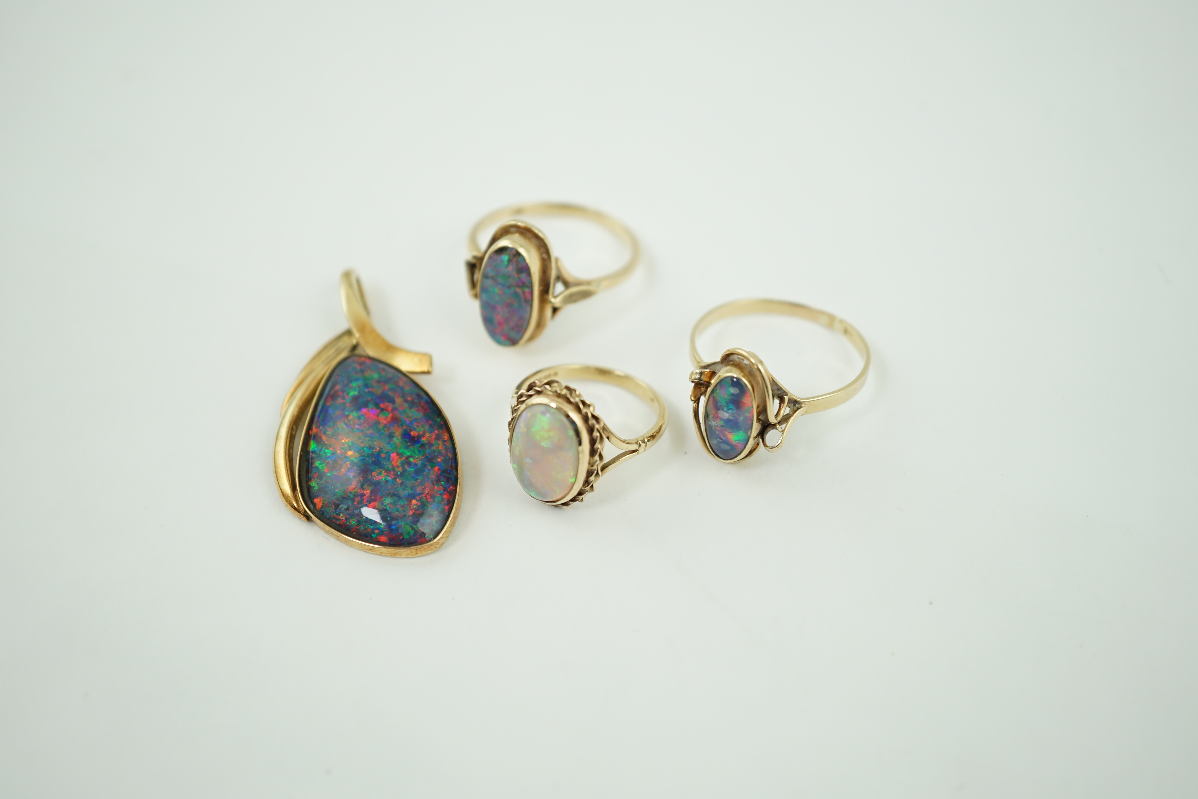 A modern 14k gold and black opal set pendant, 44mm, together with three assorted 9ct gold and single stone cabochon opal set rings